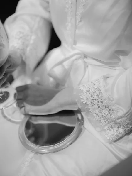 Bridal robe detail with lace trim accent and satin sash beside a handheld mirror, arranged neatly on a tabletop surface
