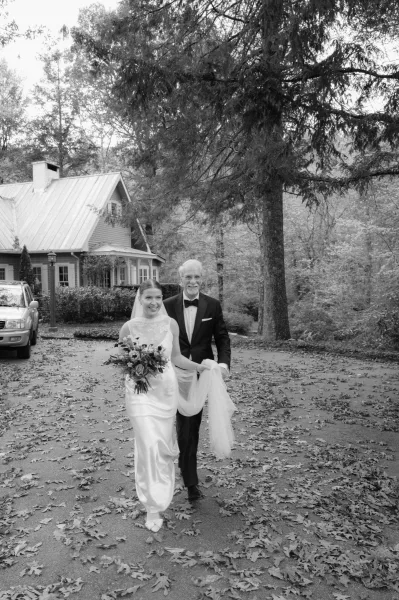 Bride with father walking arm in arm, father daughter wedding portrait with bouquet and long veil on a tree-lined driveway with fall leaves