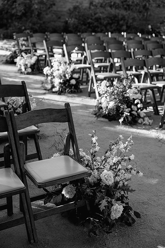Ceremony aisle decor with outdoor ceremony seating, folding chairs lining a dirt garden path with white roses and greenery clusters