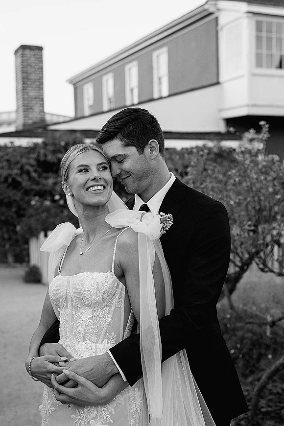 Couple portrait in a black and white wedding portrait, groom hugging bride as he kisses her forehead outside an estate building walkway