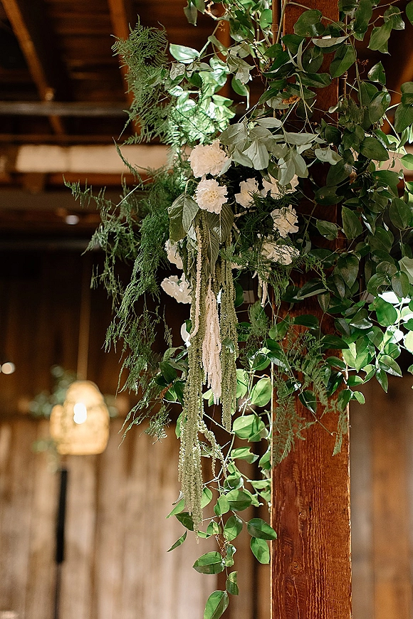 Wedding floral installation with greenery wedding decor, white flowers and cascading amaranthus draped from a rustic barn wood beam