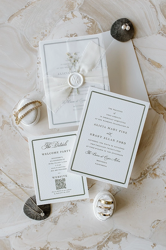 Invitation suite with wax seal and silk ribbon, styled with baby’s breath, rings, and jewelry on a marble surface flat lay