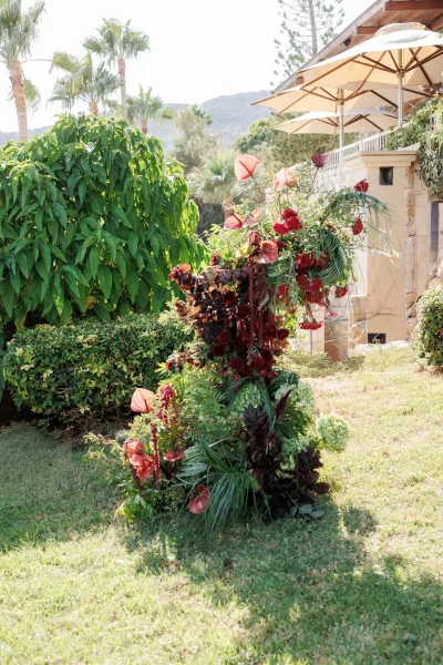 Wedding floral installation with outdoor floral arrangement of anthurium, hydrangea, greenery and palm fronds on a lawn by palm trees