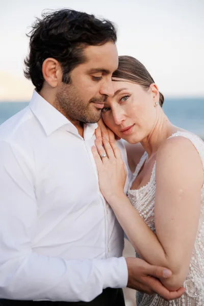 Couple portrait showing bride resting her head on groom, engagement ring on his chest, with ocean horizon in the background