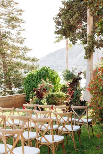 Outdoor ceremony setup with wedding ceremony seating of wood crossback chairs and white aisle runner, framed by trees and mountain views