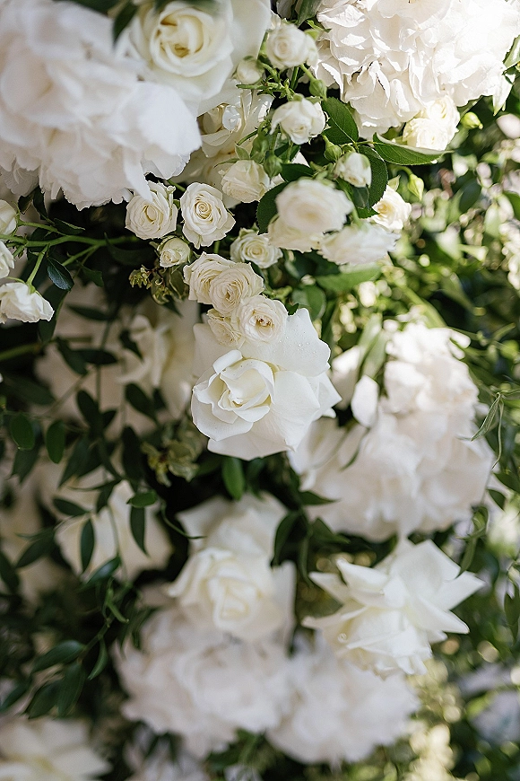 Wedding floral arrangement of white wedding flowers with roses, peonies, and greenery foliage, sunlit against lush outdoor garden greenery