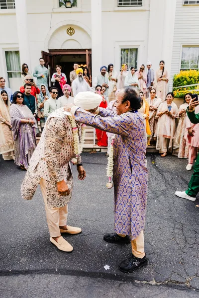 Wedding garland ceremony with Indian wedding varmala as guests crowd around a groom in turban and sherwani outside a white-columned entrance