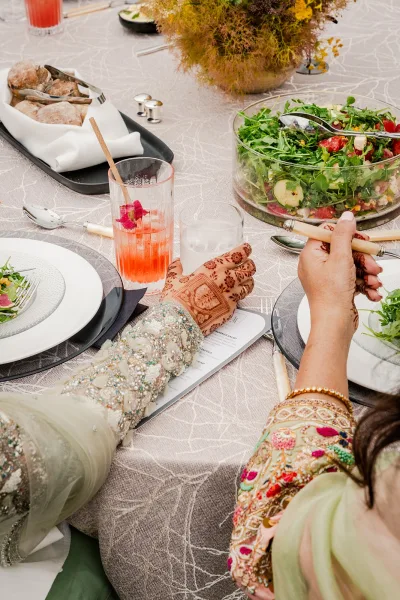 Wedding reception tablescape with wedding place setting, black and white plates, gold flatware, menu card, floral centerpiece, and henna hands reaching in
