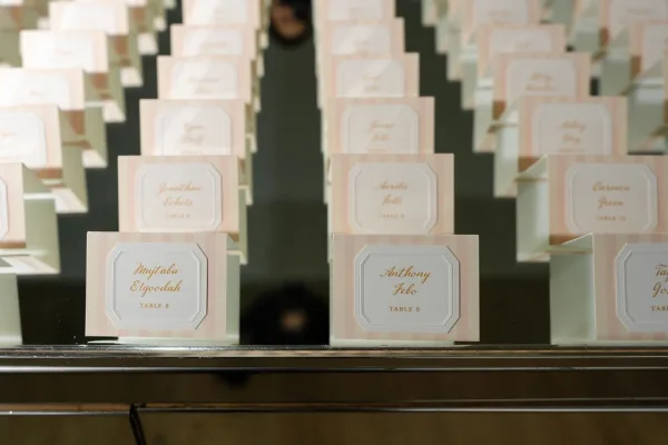 Escort card display of wedding place cards in gold lettering arranged on a mirror tabletop, neatly aligned in rows.