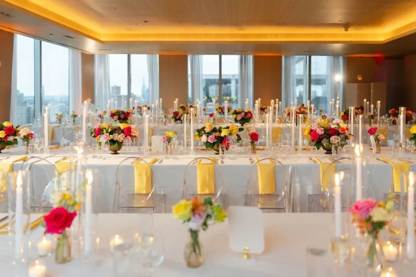 Reception tablescape at a colorful wedding reception, with floral centerpieces set before floor-to-ceiling windows revealing the city skyline.