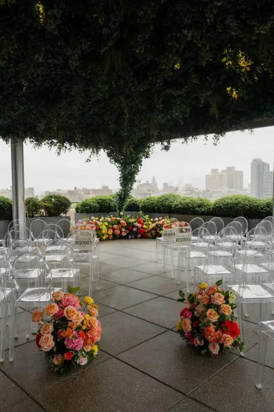 Ceremony setup showcasing rooftop ceremony decor with acrylic chairs, set on a terrace overlooking a city skyline under an overcast sky.