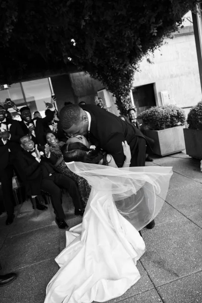 Ceremony kiss moment captured as a wedding dip kiss, the groom lowers the bride with a flowing veil while guests cheer along the aisle.