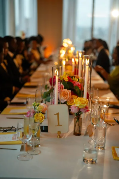 Reception tablescape as a candlelit wedding table with taper candles, framed by seated guests and a city view through windows.