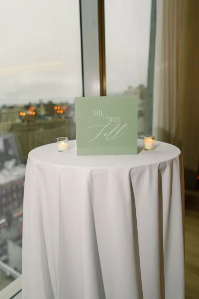 Mr and Mrs sign as a sleek acrylic wedding sign on a cocktail table with votive candles, set before a window framing the city skyline.