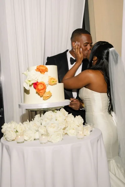 Wedding cake cutting with a cake cutting kiss as the bride and groom cut a smooth buttercream cake at a candlelit cake table.