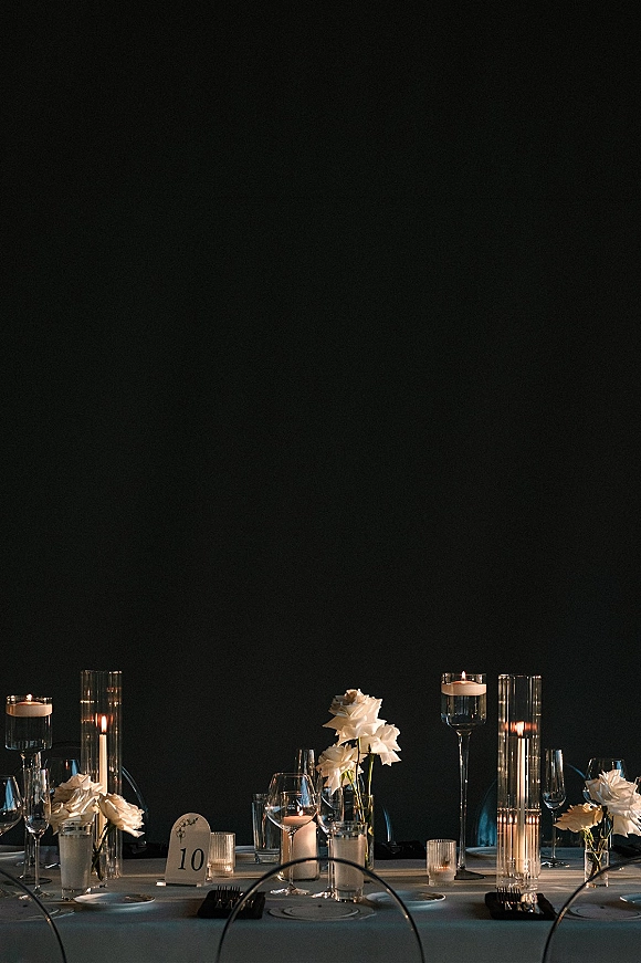 Reception tablescape with modern wedding tablescape styling, white floral centerpieces, taper and floating candles in glass vases against a dark wall backdrop