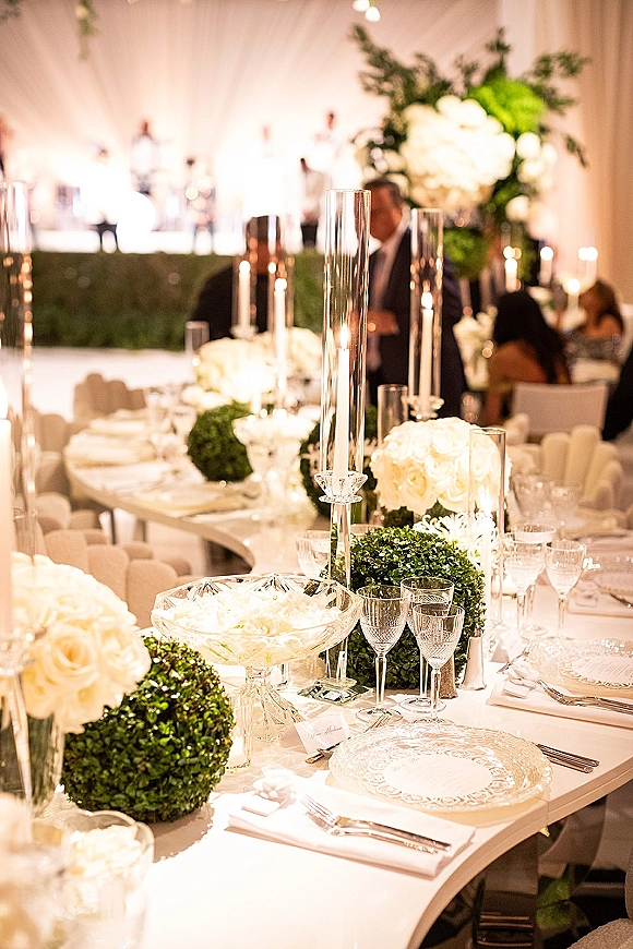 Reception tablescape with white wedding tablescape details, tall glass cylinder candles and white roses under a draped tent ceiling