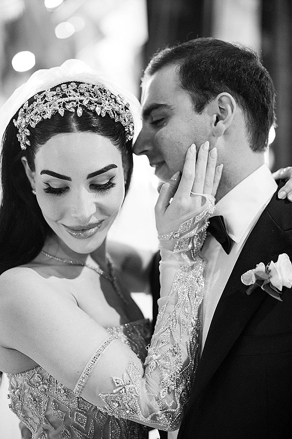 Couple portrait in a black and white wedding portrait style, groom whispering to bride as her gloved hand rests on his face under soft indoor lights