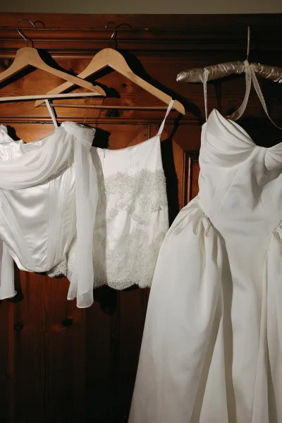 Wedding dress on hanger with lace bodice and beaded details, draped sleeves and spaghetti straps against a wood paneled wall