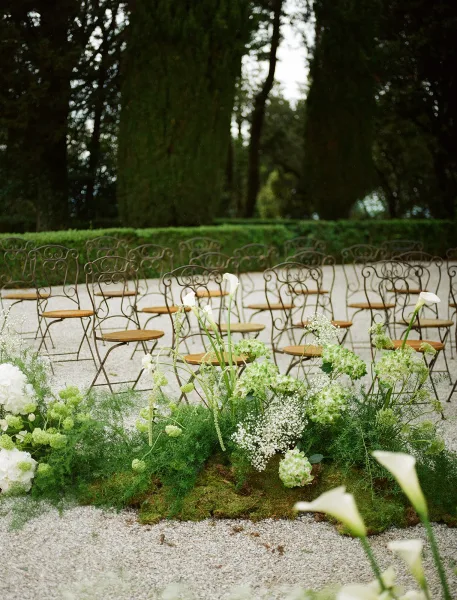Ceremony aisle decor with wedding aisle flowers in green and white, a low ground floral installation lining a gravel courtyard with wrought iron chairs