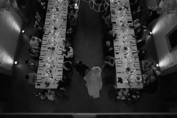 Wedding reception tables with long banquet layout, white tablecloths, taper candles, and floral centerpieces under chandeliers and hanging garlands