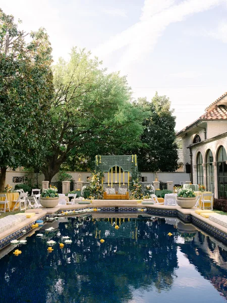 Poolside wedding decor elevates outdoor reception decor with floating flowers by a swimming pool and framed by garden trees.