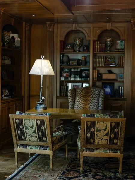 Library lounge decor with vintage library seating featuring a wingback chair, set against wood-paneled built-in bookshelves with framed photos.