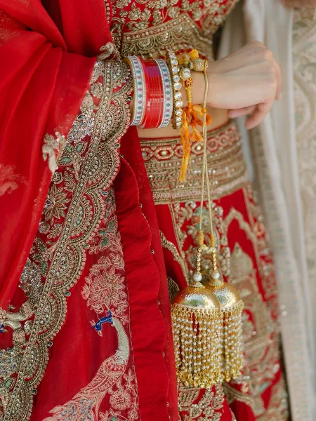 Bridal kalire dangling from red chooda bangles, set against red lehenga fabric with intricate gold threadwork embroidery.