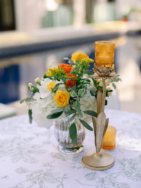 Cocktail table decor with a yellow rose centerpiece in a mercury glass vase, styled on a poolside patio.