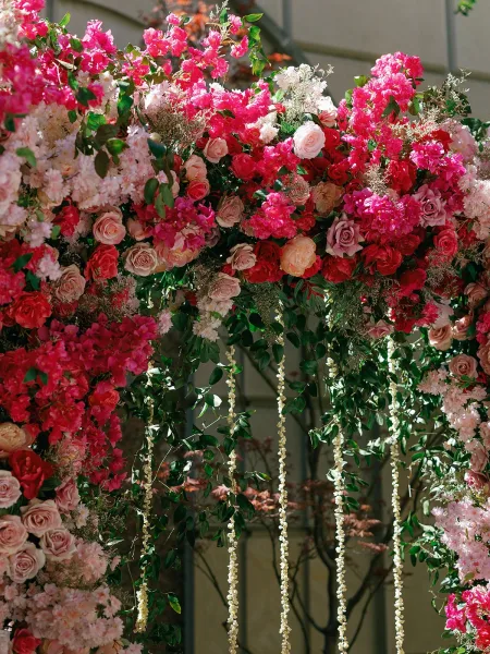 Floral wedding arch rich with ceremony backdrop florals, featuring bougainvillea, frames vows in natural light against a garden wall.