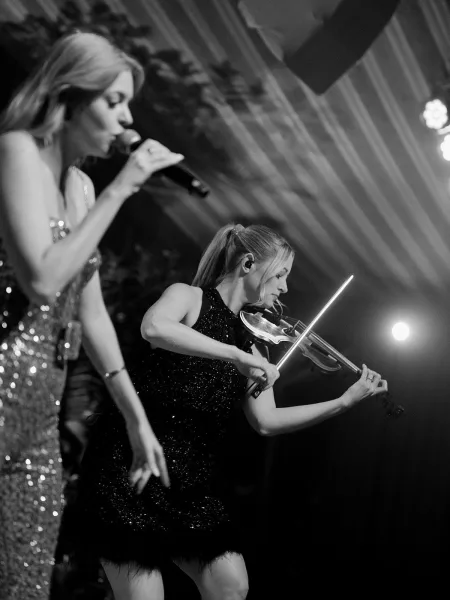 Wedding band performance featuring a female wedding singer leading with a microphone as a violinist accompanies her.