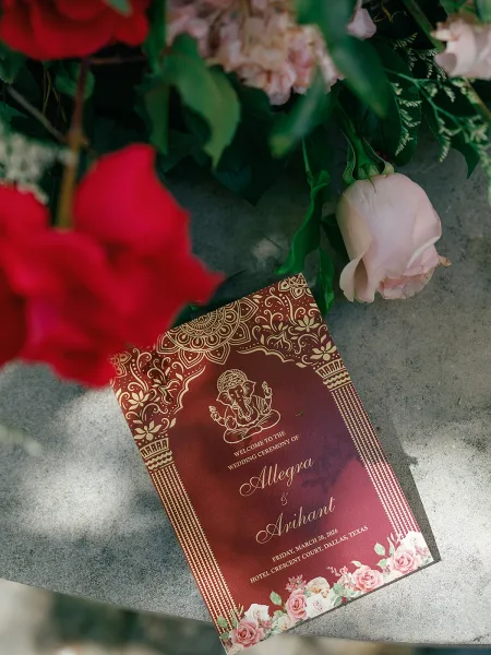 Wedding program, a Hindu wedding program featuring a Ganesha motif, styled on a stone tabletop with garden greenery in the background.