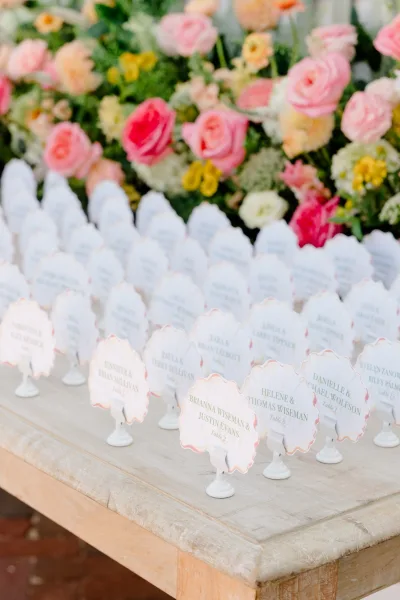 Escort card display of wedding seating cards neatly arranged in rows, accented by roses, creating an elegant, organized welcome for guests.