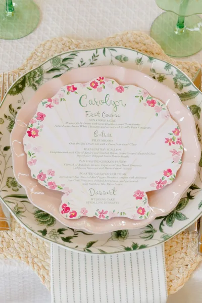 Place setting with a shell menu card centered on layered plates, arranged in a refined, symmetrical layout for a formal table presentation.