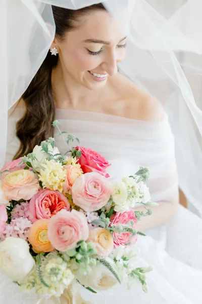 Bridal bouquet, a lush garden rose bouquet, rests under a sheer bridal veil against a white lace backdrop.