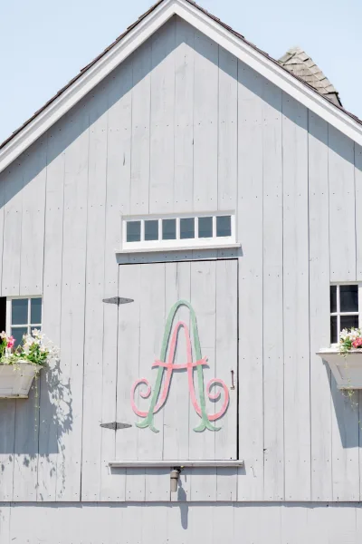 Wedding monogram displayed as a painted monogram sign on rustic barn wood siding and door, framed by florals beneath a blue sky