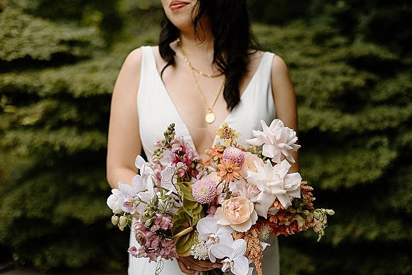 Bridal bouquet with a colorful bridal bouquet of pastel blooms and greenery held against a white wedding dress, garden foliage behind
