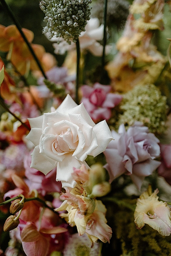 Wedding floral arrangement with a white rose centerpiece and pastel pink and peach blooms, with soft greenery and blurred florals behind