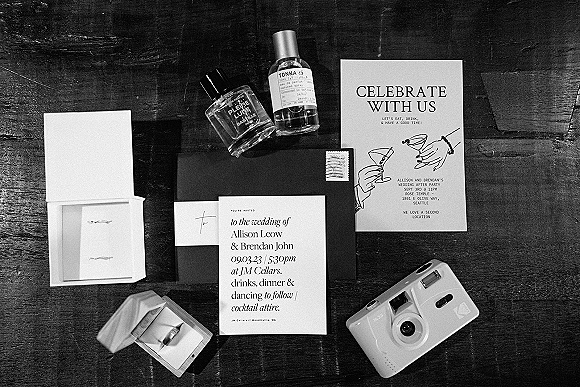 Invitation suite wedding invitation flat lay with black and white cards, envelope and stamp, rings, and perfume on a dark wood table