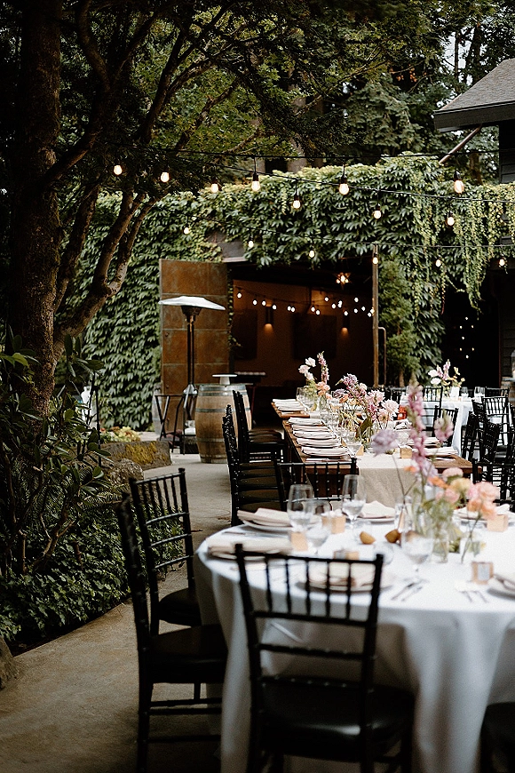 Outdoor reception tablescape with string lights wedding reception over long banquet and round tables, floral centerpieces, and an ivy-covered wall backdrop