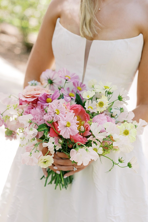 Bridal bouquet in a garden style bridal bouquet of peach roses, pink and white cosmos, and greenery held by a bride on a sunlit garden path