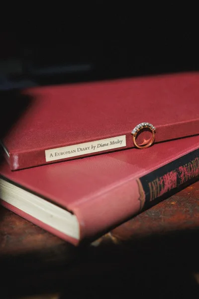 Wedding rings with a diamond halo engagement ring and gold band stacked on a hardcover book atop a wood surface against a dark backdrop