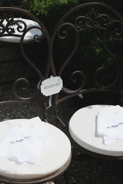 Reserved wedding seating with reserved chair sign and lace ribbon on wrought iron chairs, white cushions and embroidered handkerchiefs outdoors