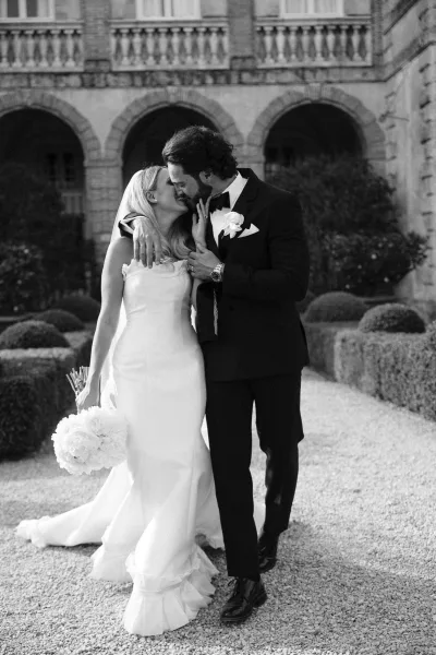 Wedding kiss portrait of bride and groom kissing under stone arches, her veil flowing as he holds her close in a garden courtyard