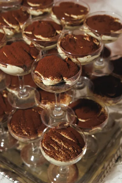 Wedding dessert cups of tiramisu dessert cups in glass coupe cups, layered cream with cocoa dusting on a silver tray at a dessert table