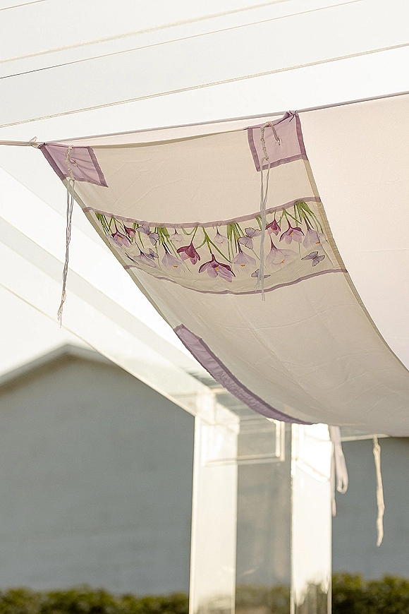 Wedding canopy draping with sheer tent draping panels, floral embroidery and lavender trim hanging beneath a bright tent ceiling