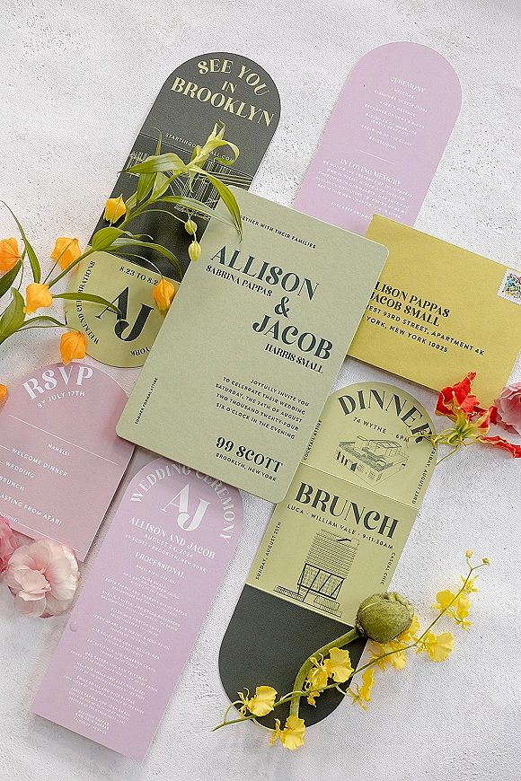Wedding invitation suite with modern wedding invitations arranged as a flat lay of cards, envelopes, postage, and floral buds on white texture