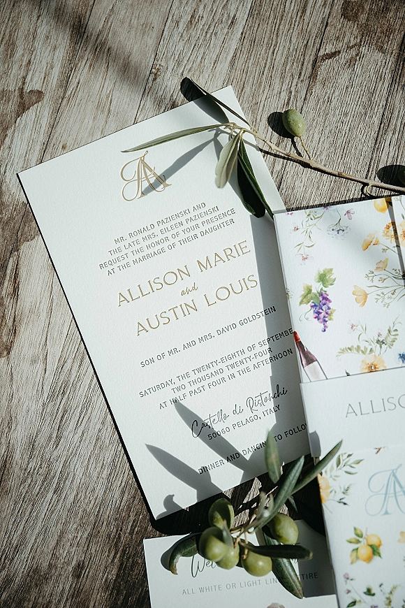 Wedding invitation suite with letterpress wedding invitations, olive branch accent and floral liner envelope on a weathered wood table in sunlight