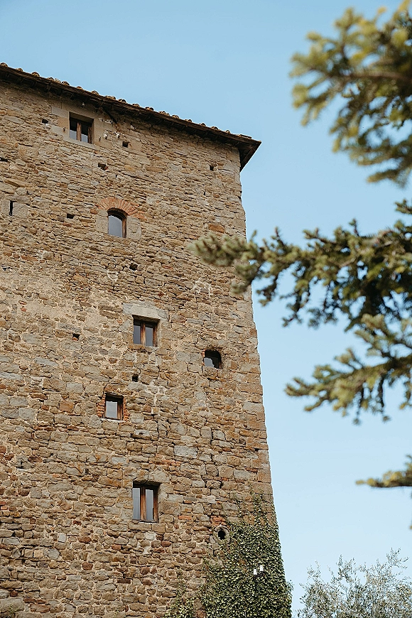 Stone wedding venue with ivy climbing the historic facade, framed by bare tree branches against a clear blue sky