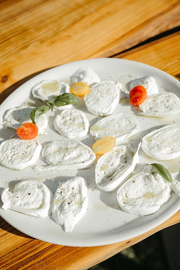 Mozzarella appetizer plate with caprese appetizer platter styling, fresh mozzarella, basil and cherry tomatoes, drizzled olive oil on a wood table